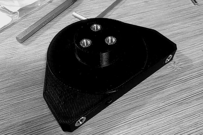 Additively manufactured mount with a raised boss and heat-set brass threaded inserts.
